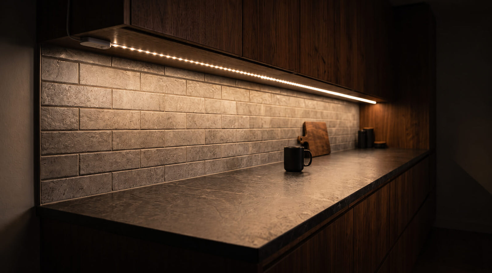 A warm light strip under a kitchen cabinet, lighting a stone counter at night